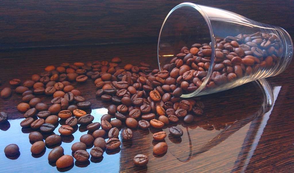 Зерна кави розсипані по столу зі склянкою